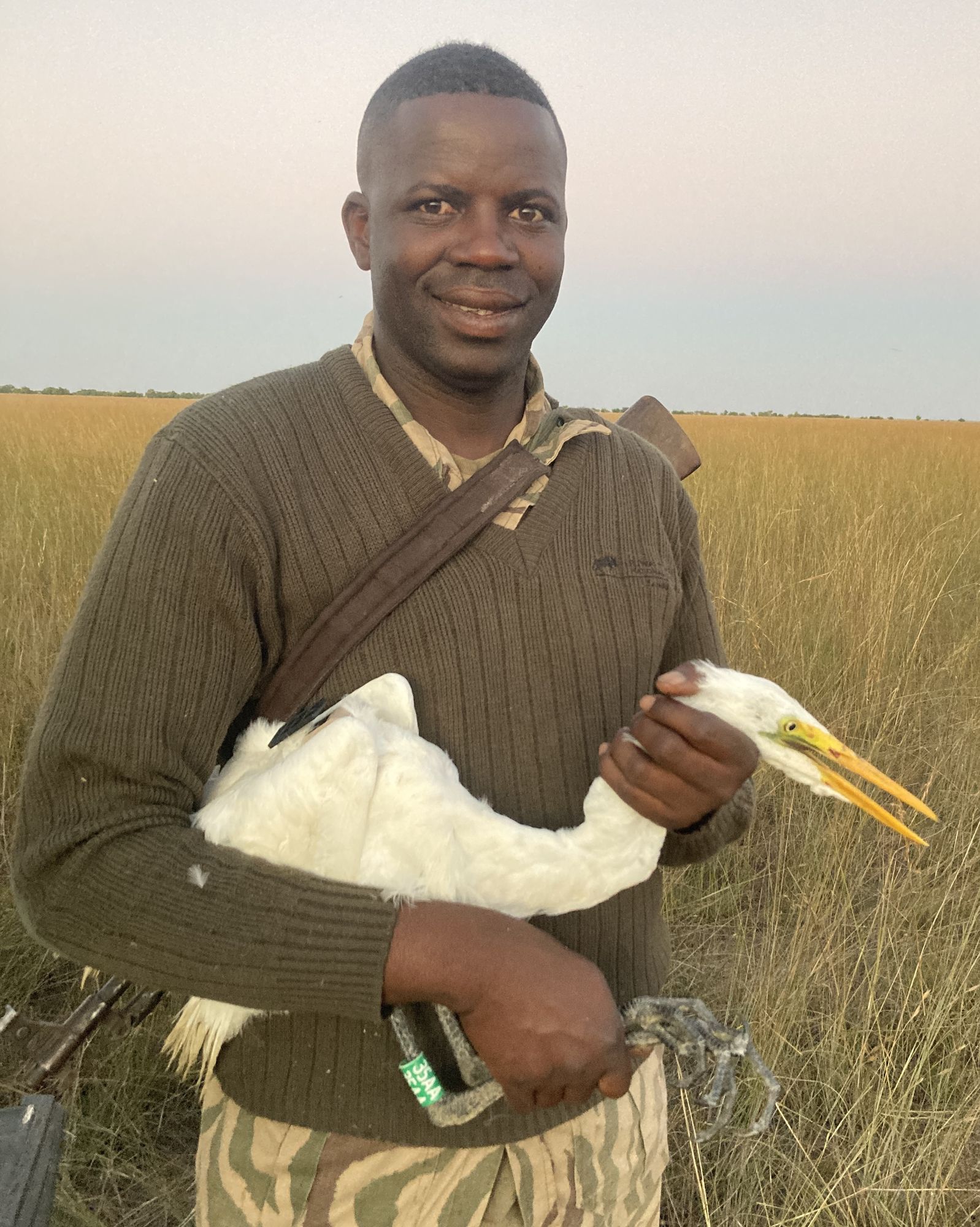 Amukena Mungole holding an egret in tall grass
