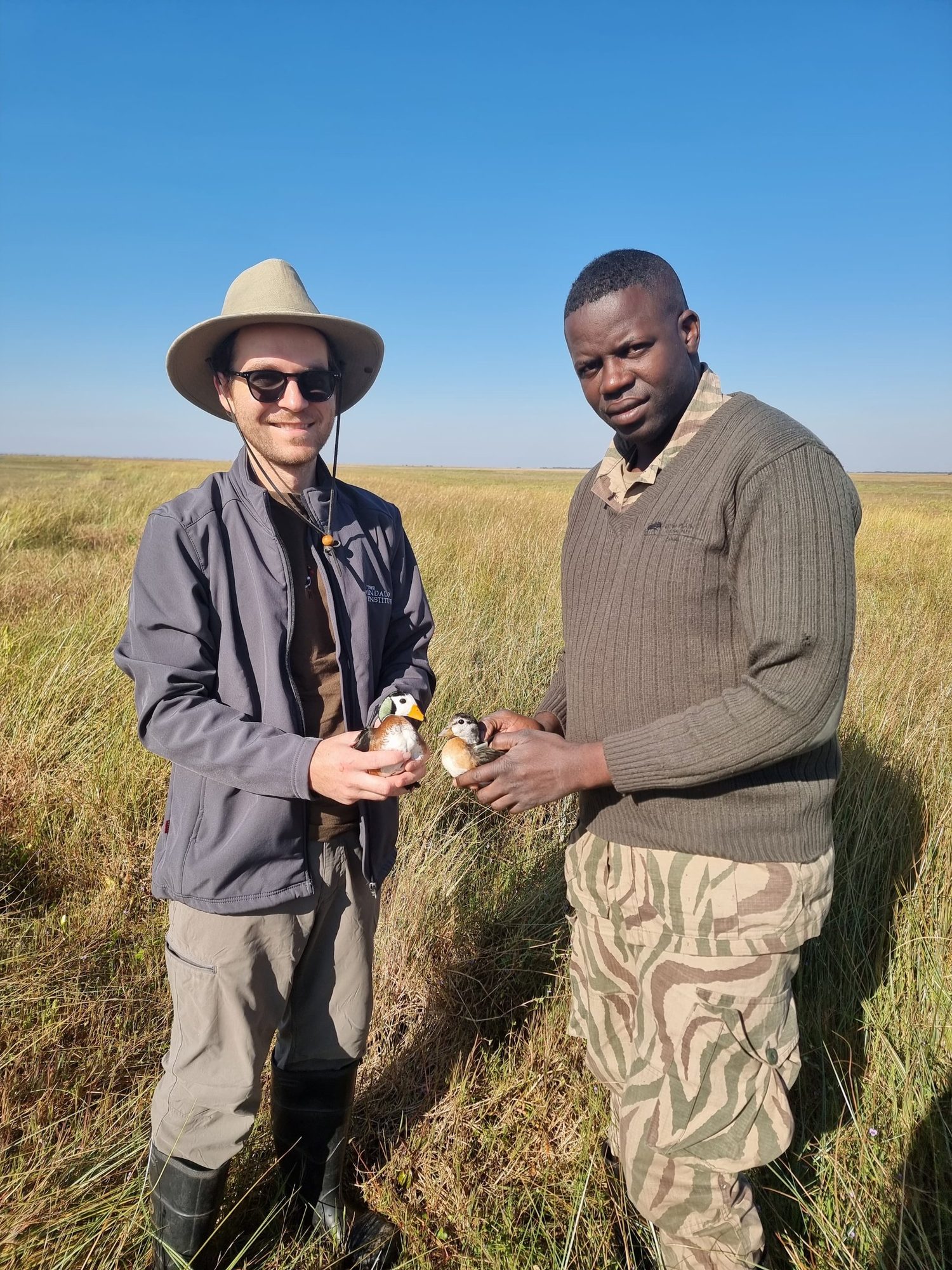 Dr Jonah Gula and Amukena Mungole holding African Pygmy Geese on a floodplain